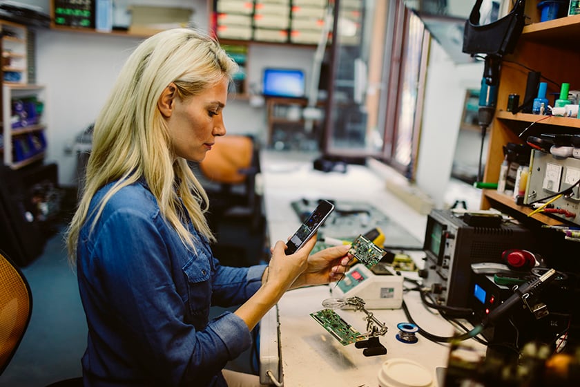 Mujer mirando el teléfono mientras repara un equipo