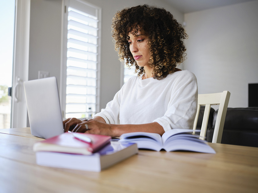 Estudiante con libros académicos abiertos mirando un portátil